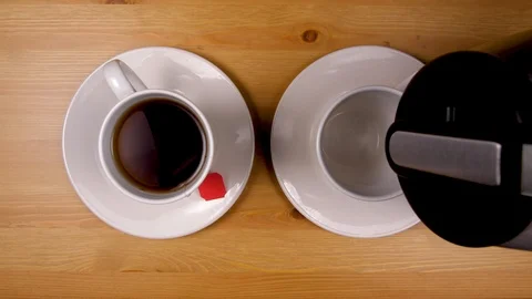 Hand pouring coffee beside tea cup on wood table top down Stock Footage 86876802