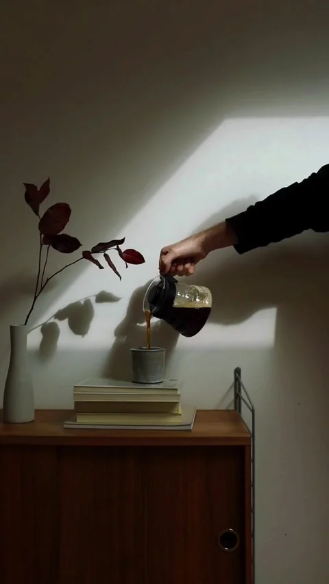 Hand pouring fresh black coffee from glass carafe in cozy home interior Video stock 344851182