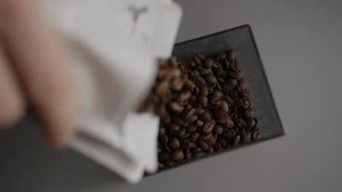 Hand pouring fresh roasted coffee beans from white bag into gray container for Stock Footage 342755783