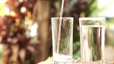  hand pouring fresh water on drinking glass over nature sunlight morning Stock Footage