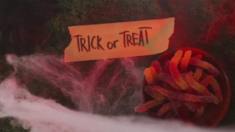 Hand pouring gummy worms over Trick or Treat sign in red light Stock-Footage 342520439