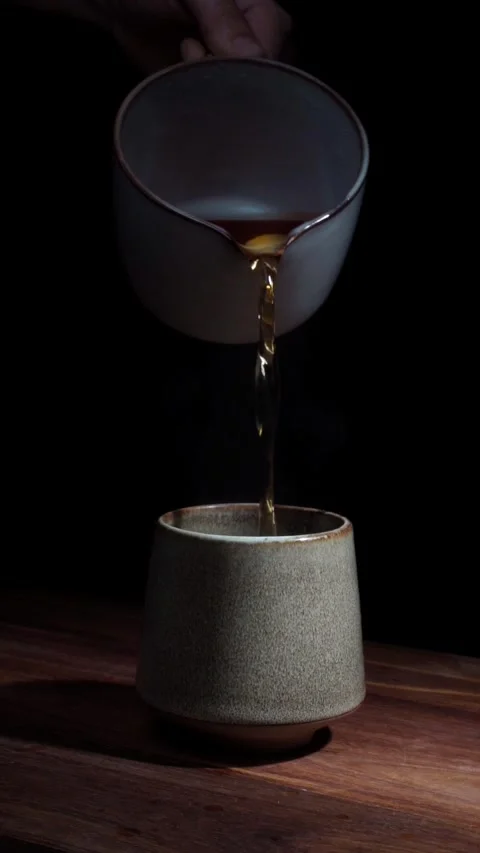 Hand pouring hot tea into ceramic cup steam dark background vertical Stock Footage 324761959
