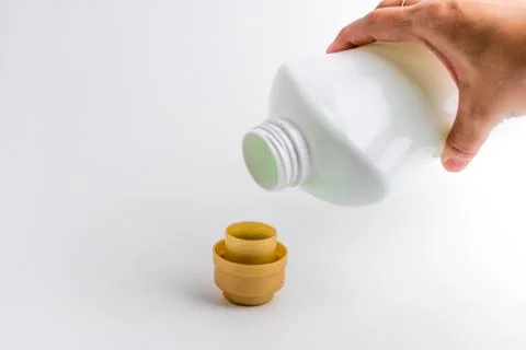 Hand pouring liquid laundry detergent from white plastic bottle into cap Stock Photos