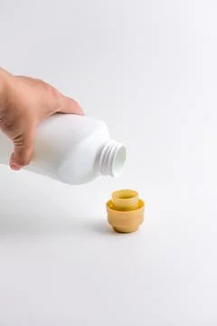 Hand pouring liquid laundry detergent from white plastic bottle into cap Stock Photos