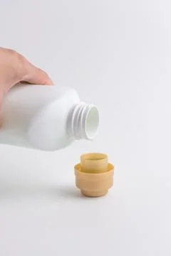 Hand pouring liquid laundry detergent from white plastic bottle into cap Stock Photos