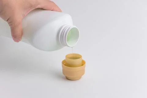 Hand pouring liquid laundry detergent from white plastic bottle into cap Stock Photos