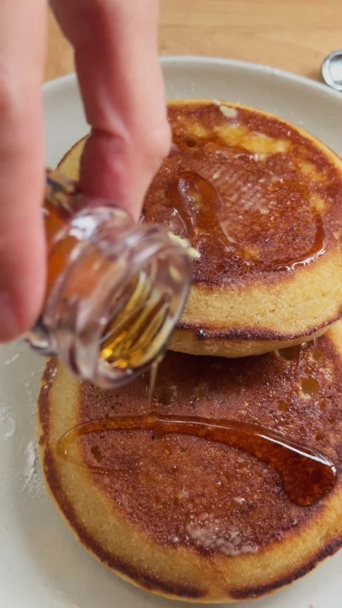 Hand pouring maple syrup over stack of fluffy pancakes with butter Video stock 338246306