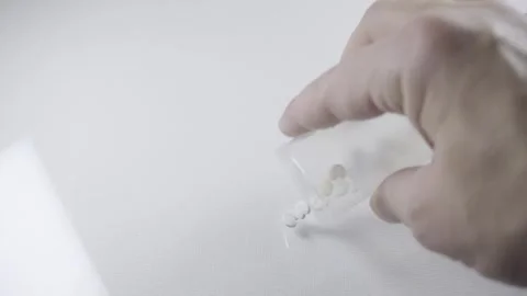 Hand pouring pills from transparent pill bottle onto white background close u Vídeos de archivo 342838845