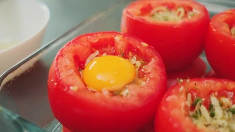 Hand Pouring Raw Egg into Cheese-Stuffed Tomatoes in Kitchen Видео 342878140