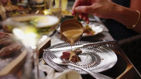 Hand Pouring Sauce Over Steak at Elegant Dinner Table With Wine and Side Dishes Stock Footage 342286388