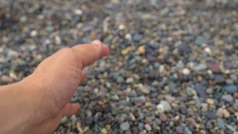 Hand pouring small smooth pebbles onto a stone beach Stock Footage 342077801