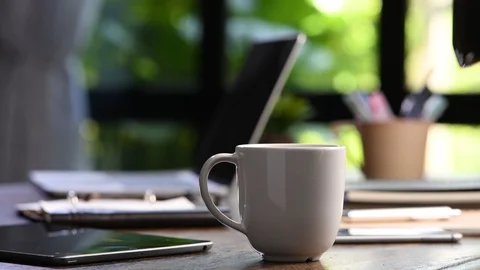 A hand pouring steaming coffee in to a cup on a work desk when work from home 库存影片 127333735