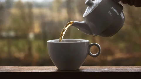 A hand pours aromatic tea from a teapot into a mug in rainy weather outdoors. Stock Footage 147674305