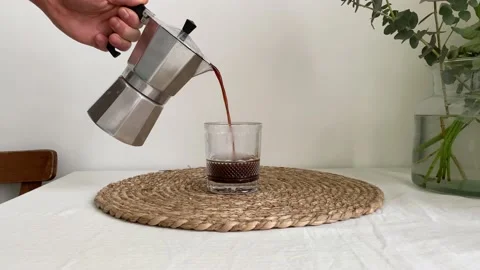 Hand pours fresh hot coffee from silver steel moka pot into glass cup 動画素材 150782852