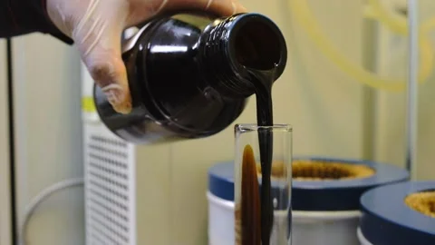 The hand pours a sample of black oil from a bottle into a flask Stock Footage 221084871