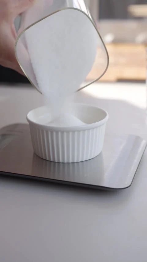 Hand pours sugar into a bowl on kitchen scale. Concept of measuring ingredients Stock Footage 336753789