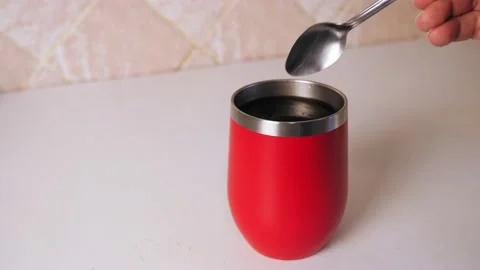 A hand pours sugar into a red mug with hot tea. Teaspoon with a mountain of Stock Footage 224790144
