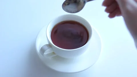 The hand pours a teaspoon of sugar into the tea and stirs. Stock Footage 168935147