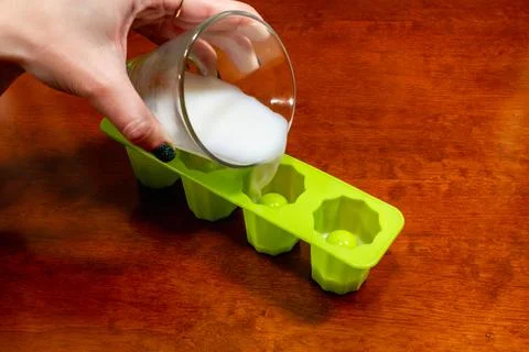 Hand pours white liquid into green silicone star mold tray on wood table. Foto stock