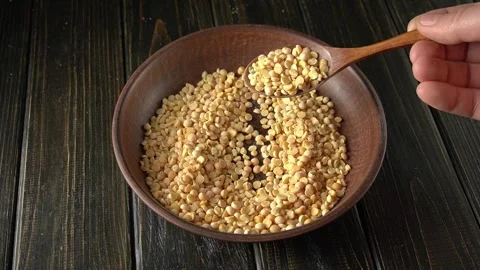 A hand pours yellow split peas from a wooden spoon into a clay bowl, Video stock 330407526
