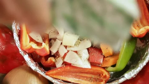 Hand prepares vegetables for roasting by adding spices to foil-lined dish with Stock Footage 318969686
