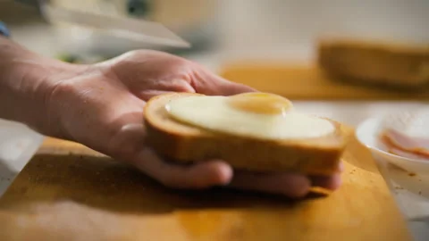 Hand preparing a breakfast dish with egg and bread in a casual kitchen setti Stock Footage 304276617