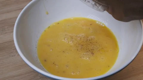 Hand preparing breakfast mix eggs in a bowl for homemade omelettes and seasoning Stock Footage 172424956