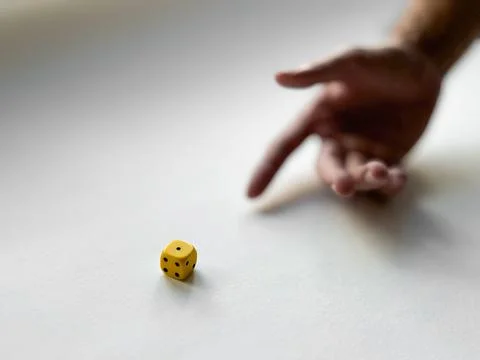 Hand preparing to roll yellow dice on minimalist white background Stock Photos