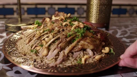Hand Presenting Lamb Rack with Rice and Nuts on Ornate Platter in Traditional Stock Footage 345953231