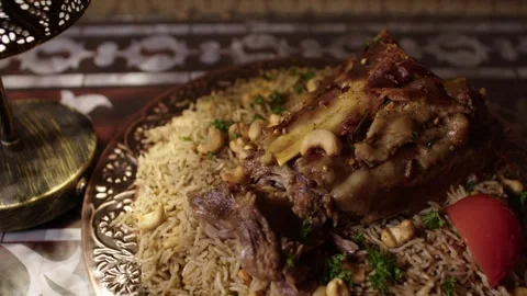 Hand Presenting Traditional Lamb and Rice Dish with Nuts on Ornate Plate Indoors Stock Footage 345954083