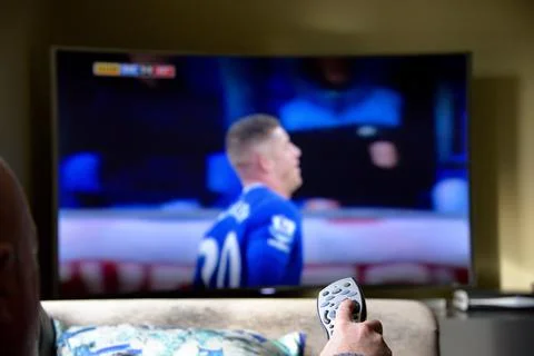 Hand presing a button on the remote control in front of a television Stock Photos