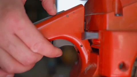 The hand presses the accelerator button on the handle of an orange chainsaw Stock Footage 207621986