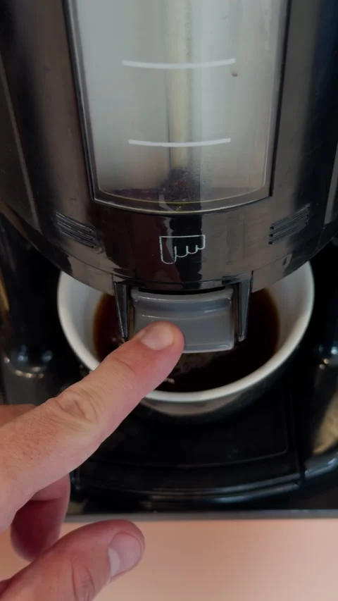 Hand presses coffee dispenser lever above cup with fresh brew and foam inside Stock Footage 344966703