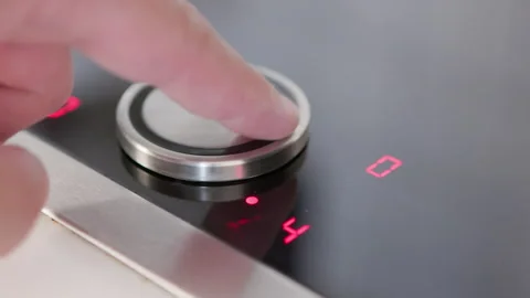 A hand presses the control of a sleek modern induction cooktop with glowing indi Stock Footage 281595607