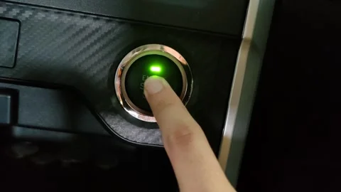 A hand presses the illuminated engine start button on the dashboard of a car Stock Footage 304072780