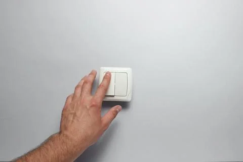 Hand presses a light switch on gray wall background Stock Photos