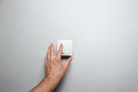 Hand presses a light switch on gray wall background Stock Photos
