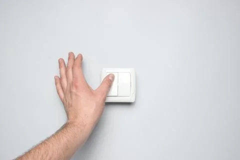 Hand presses a light switch on gray wall background Stock Photos