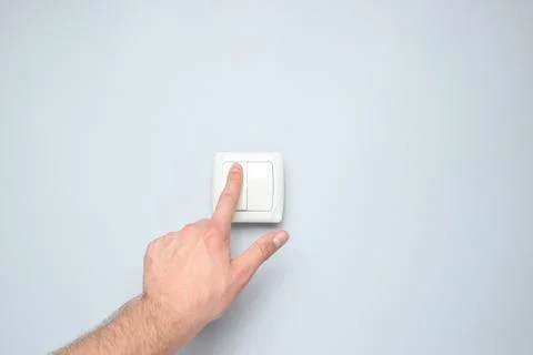 Hand presses a light switch on gray wall background 写真素材