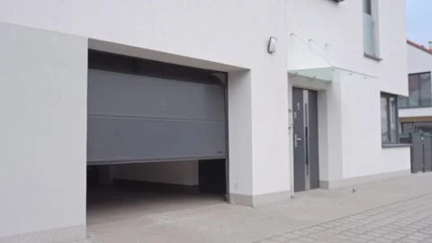 Hand presses remote control while holding house keys in front of closed garage Stock Footage 330073854