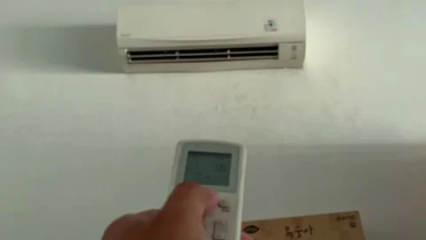Hand pressing air conditioner remote button to switch on and controlling room Stock Footage 344011424