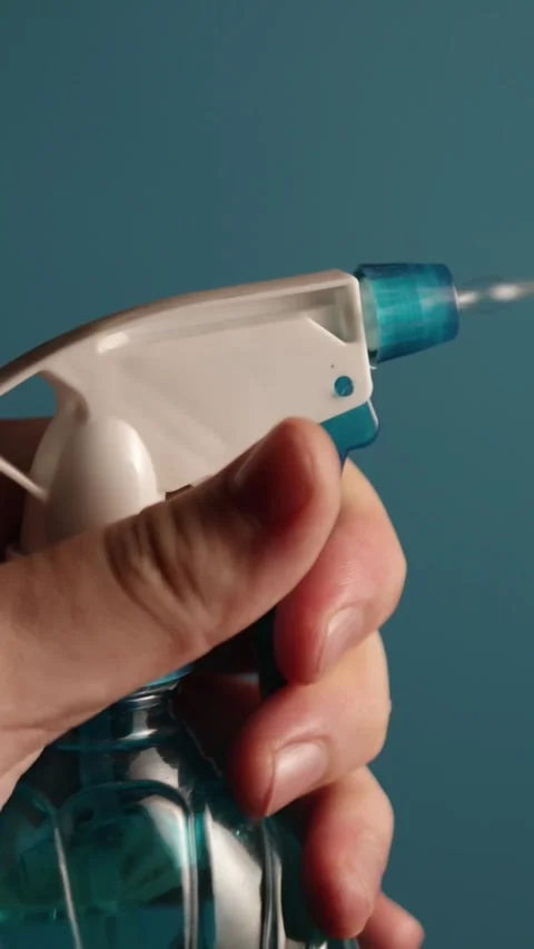 Hand pressing blue spray bottle trigger releasing fine mist against blue Vidéo 343838191