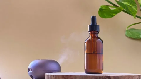 Hand pressing button on aroma diffuser blowing steam near amber bottle. Stock Footage 337100958
