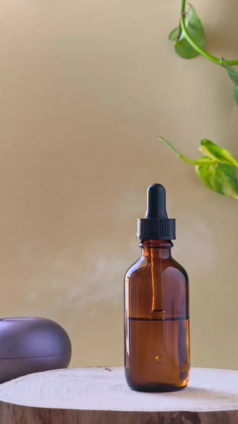 Hand pressing button on aroma diffuser blowing steam near amber bottle. Video stock 337101010