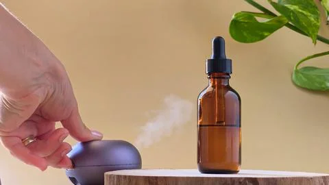 Hand pressing button on aroma diffuser blowing steam near amber bottle. Stock Photos
