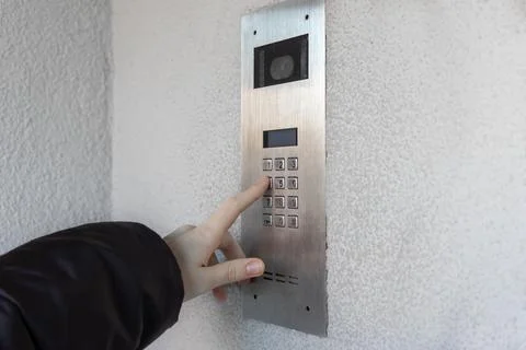 Hand pressing button on modern intercom keypad with camera on textured white  Stock Photos