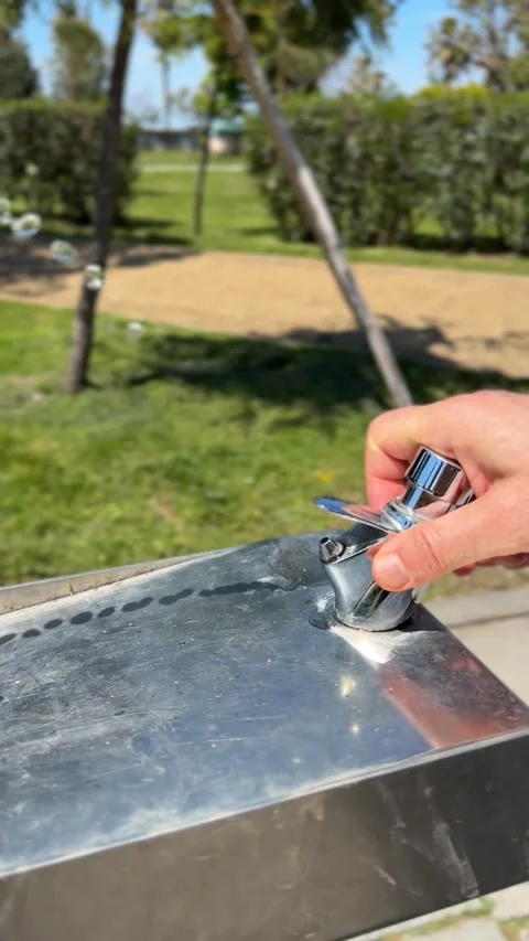 Hand pressing button on outdoor water fountain spout with stream against pa.. Stock Footage 337027388