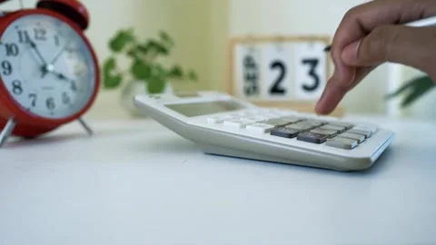 Hand pressing buttons on a calculator with a clock and calendar in the back.. Stock Footage 320725298