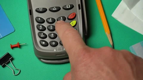 Hand pressing buttons on a payment terminal with office supplies like a pencil, Stock Footage 334252059