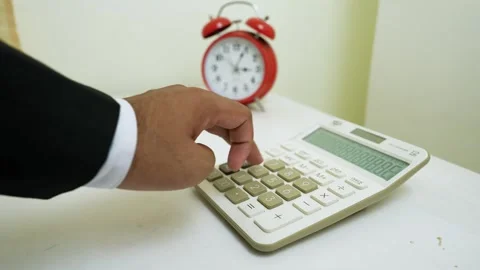 Hand Pressing Calculator with Alarm Clock Nearby Stock Footage 320725640
